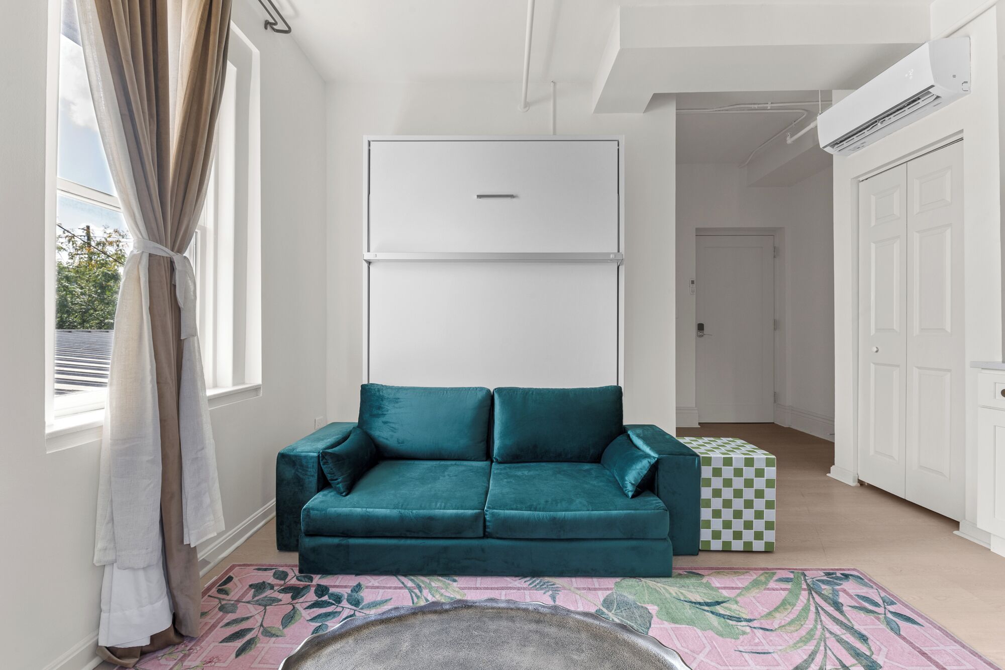 Een smaragdgroene bank in een lichte kamer met een wit plafond, een geruit doos en een vloerkleed met dessin.