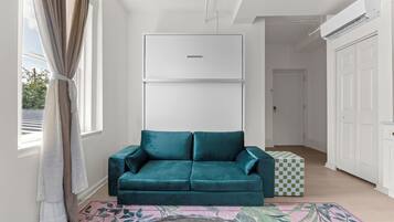 Un canapé de couleur turquoise dans une pièce lumineuse, avec un plafond blanc, une boîte à motifs géométriques et un tapis à motifs.