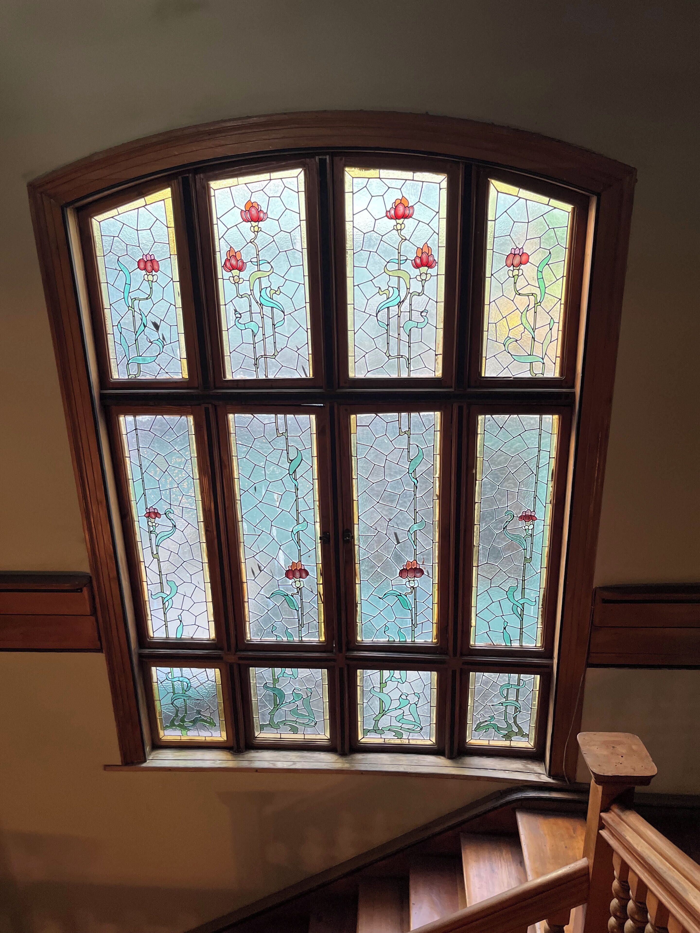 Une fenêtre d’angle ornée de vitraux représentant des fleurs et des feuilles.