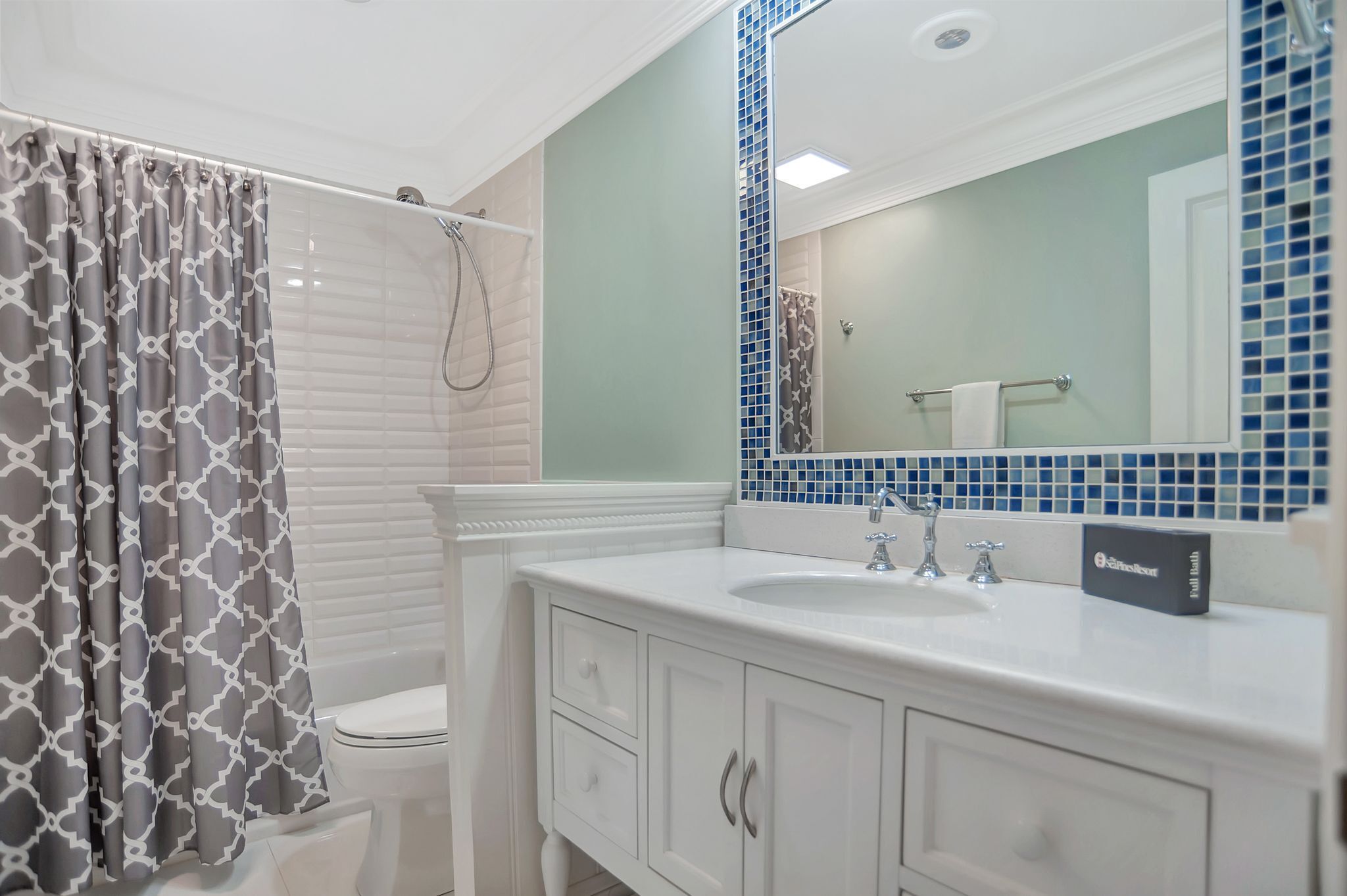 A bathroom with a white toilet, a shower with a patterned curtain, a sink with a mirror, and a towel rack.