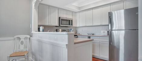 A kitchen with white cabinetry, a stainless steel refrigerator, a microwave, and a built-in island with a chair.