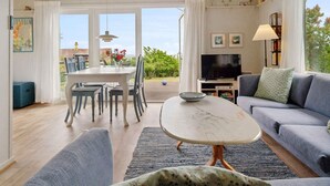 Ein geräumiges Wohnzimmer mit Essbereich, einer Couch, einem Fernseher und einem Balkon mit Aussicht.