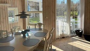 A wooden interior with a dining table set for four, a clock, and large windows overlooking a garden. - 5 Star Holiday Home in Eskebjerg (Eskebjerg)
