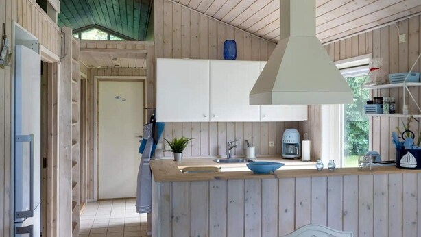 A kitchen with wooden cabinets, a central island, and a hanging light fixture. - 5 Star Holiday Home in Eskebjerg (Eskebjerg)