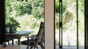 Une terrasse extérieure avec une table et des chaises, donnant sur un jardin luxuriant et bordé d’une clôture en bois.