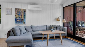Un salon moderne avec un canapé d’angle gris, une table basse en bois et un tapis à motifs bleus.
