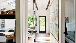 Un espace de vie lumineux et décloisonné, doté d’un plancher en bois, d’un coin repas avec une table et des chaises, et d’une grande fenêtre offrant une vue sur la verdure environnante.