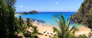 A beach with clear turquoise water, palm trees, and a rocky outcrop. - Casa Noronha Martins (Fernando de Noronha)