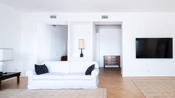 Un soggiorno minimalista con un divano bianco, un tavolino in legno, una lampada, una TV e un tappeto decorato.