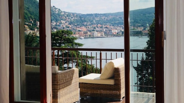 Varanda com mobiliário de vime com vista para uma paisagem urbana e um corpo de água.