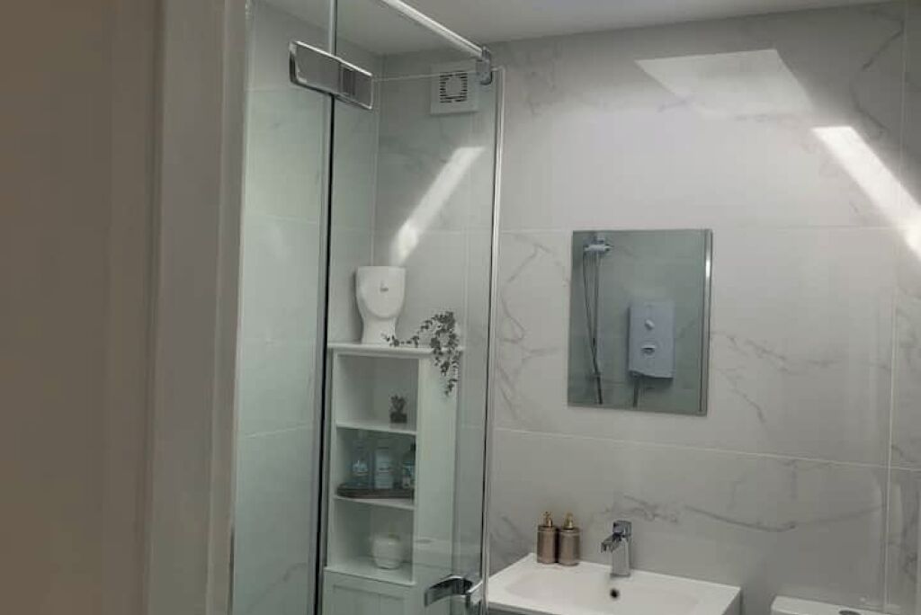 Un baño moderno con cabina de ducha de vidrio, un lavamanos blanco y un revestimiento de mármol en la pared.