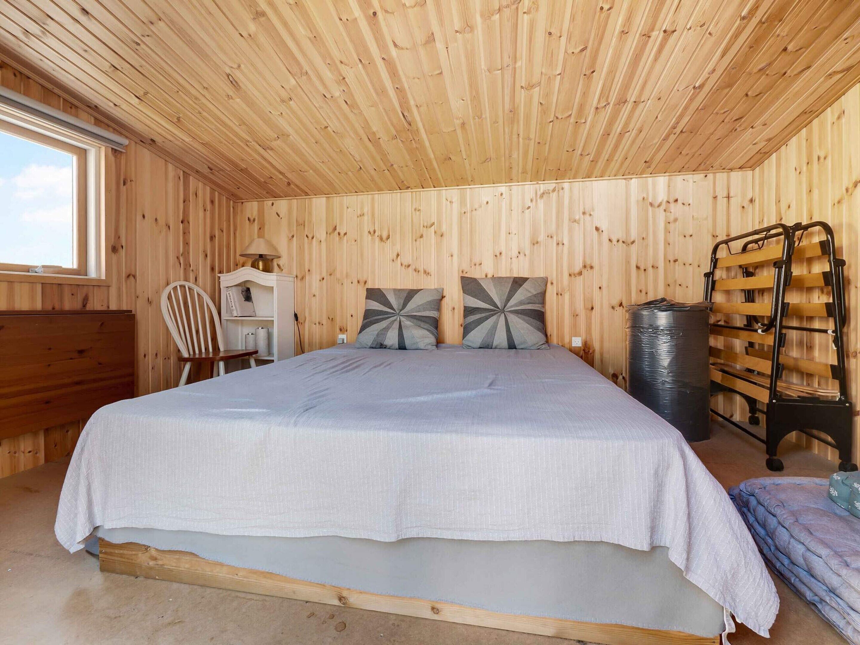 A wooden-paneled bedroom with a bed, a desk, and a chair.