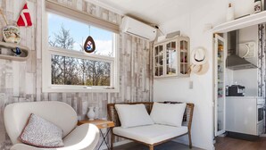 A modern living room with a white armchair, a wicker sofa, and a dining area with a cabinet. - 5 Star Holiday Home in Sjaellands Odde (Sjællands Odde)