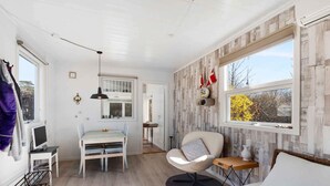A bright, well-lit room with a dining table, a sofa, and a chair. There is a window with a view of trees and a door leading to another room. - 5 Star Holiday Home in Sjaellands Odde (Sjællands Odde)