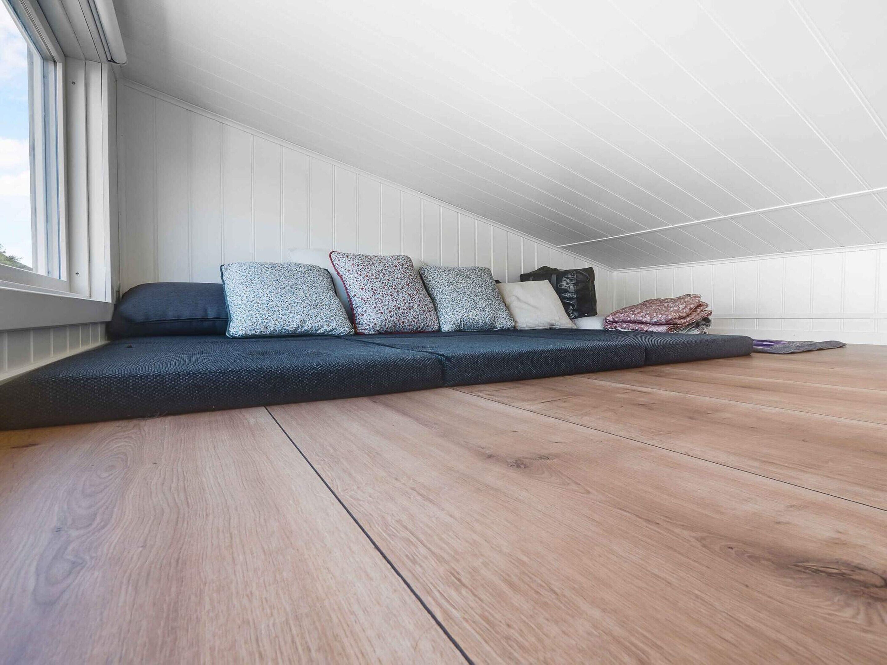 A loft bedroom with a built-in bed, wooden flooring, and a window providing natural light.