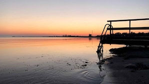 A serene sunset over a calm body of water with a distant industrial structure. - 5 Star Holiday Home in Sjaellands Odde (Sjællands Odde)