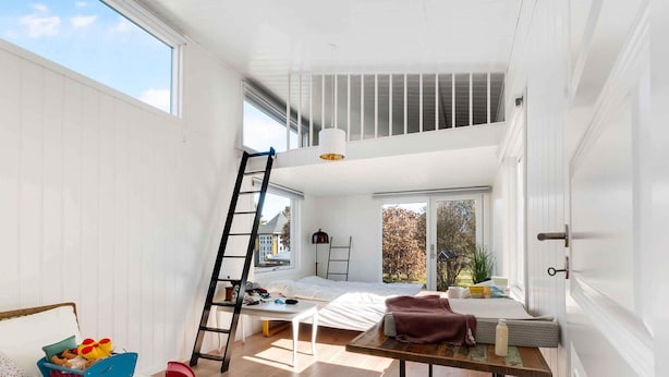 A spacious room with a loft bed, a small table, a ladder, and a window overlooking a garden. - 5 Star Holiday Home in Sjaellands Odde (Sjællands Odde)