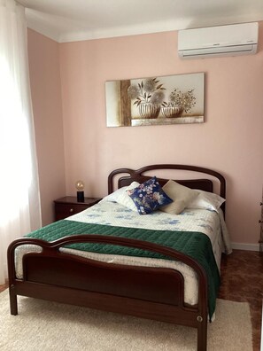 Une chambre à coucher comprenant un lit, une table de chevet, un climatiseur fixé au mur et un tableau.