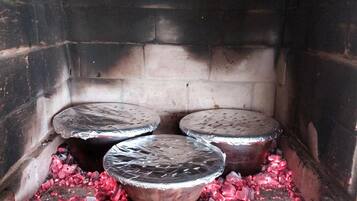 A brick oven with four metal containers on a bed of glowing coals.