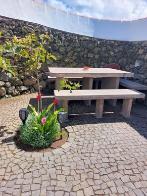 A stone patio with a picnic table, a small garden with plants and a decorative lamp, and a stone wall in the background.