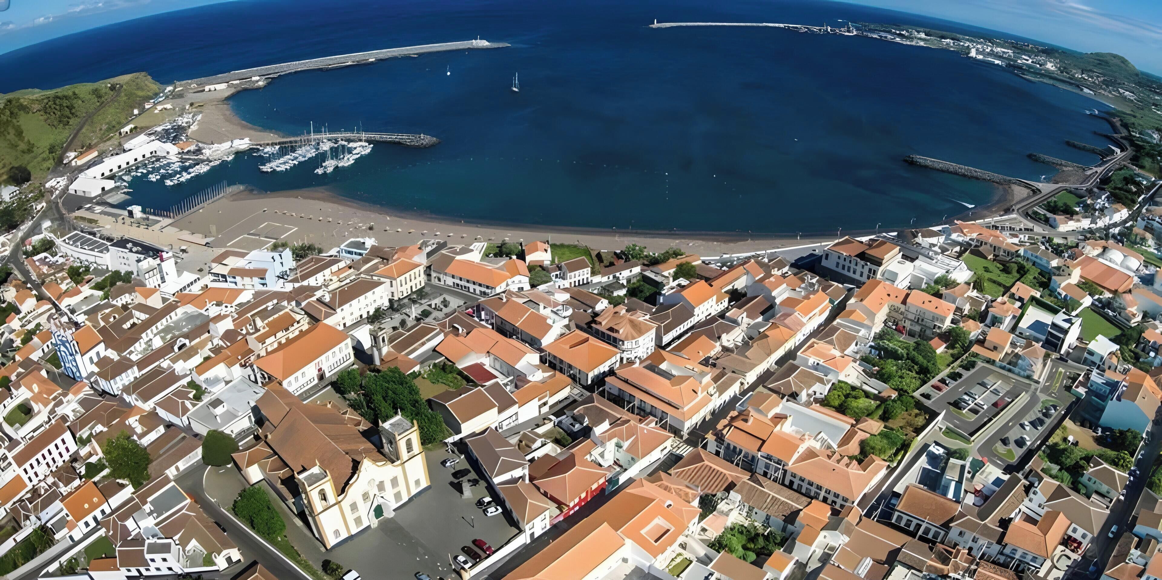 An aerial view of a coastal town with a marina, residential buildings, and a prominent church.