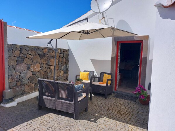 A patio with wicker furniture, a stone wall, and a door leading inside.