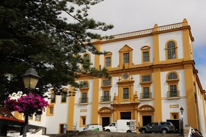 A large building with multiple windows and balconies, a staircase leading to the entrance, and a parked vehicle in front.