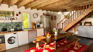 A kitchen with wooden beams, a dining table with a red floral rug, a clock, and a staircase.