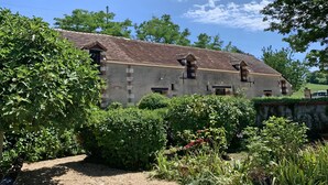 A rustic building with a tiled roof, surrounded by lush greenery and a gravel path.