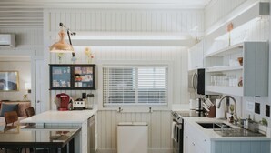 Een keuken met een centraal eiland, een inbouwoven, een koelkast en een raam met zonwering.