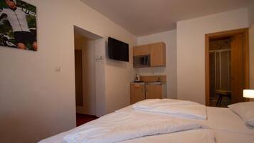 Et hotelværelse med en seng, et fjernsyn ophængt over et træskab, og et bruseområde.