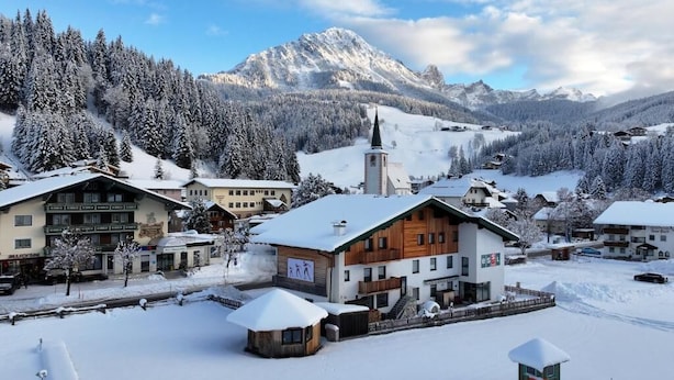 A snow-covered village with a church, wooden buildings, and a mountain backdrop.