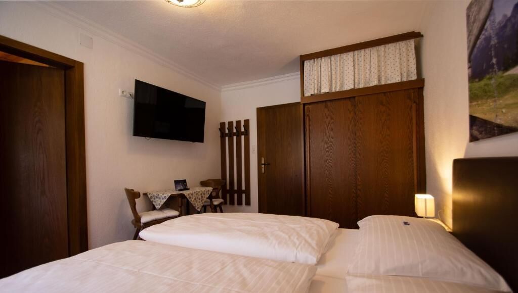 Een slaapkamer met twee bedden, een televisie, een houten kledingkast, een kleine tafel met stoelen en een tv aan de muur.