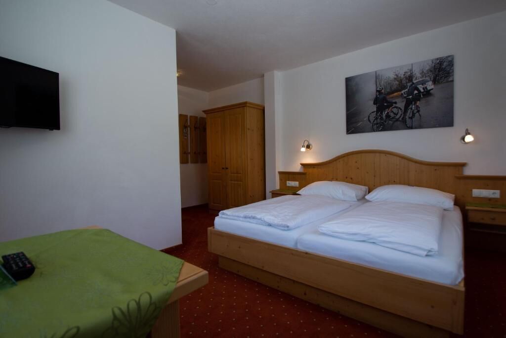 Une chambre à coucher avec un lit en bois, une table verte, un téléviseur et un tableau accroché au mur.