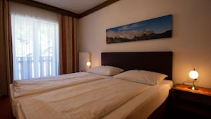 A hotel room with a bed, two bedside lamps, a window with curtains, and a painting on the wall.