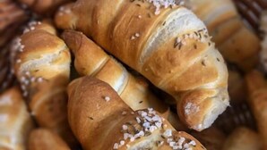 A basket of freshly baked bread rolls with sesame seeds and herbs.