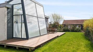 Uma casa moderna com uma ampla extensão de vidro, um deck de madeira e um gramado bem cuidado.