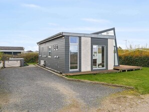 A modern, single-story house with a grey exterior, large windows, and a small deck.