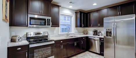 A modern kitchen with dark cabinets, stainless steel appliances, and a window with blinds.