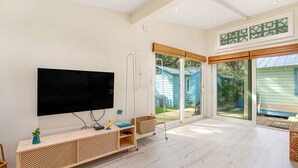 A spacious living room with a large flat-screen TV mounted on the wall, a wooden console table, and a sliding glass door leading to an outdoor area.