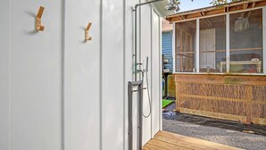 A wooden deck with a metal railing, a white door with a small window, and a wooden structure with a window and a shelf.