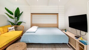 A modern bedroom with a bed, a sofa, a TV, and a plant.