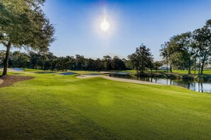 A golf course with a pond, trees, and a clear sky.