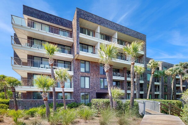 Un hotel de varios pisos con balcones, palmeras y un paseo de madera.