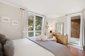 A bedroom with a bed, a dresser, a chair, a lamp, and a large window with curtains.