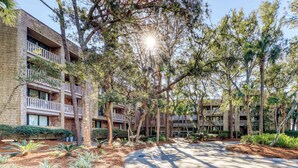 Un immeuble à plusieurs étages doté de balcons, entouré d’arbres et bordé d’une allée pavée.