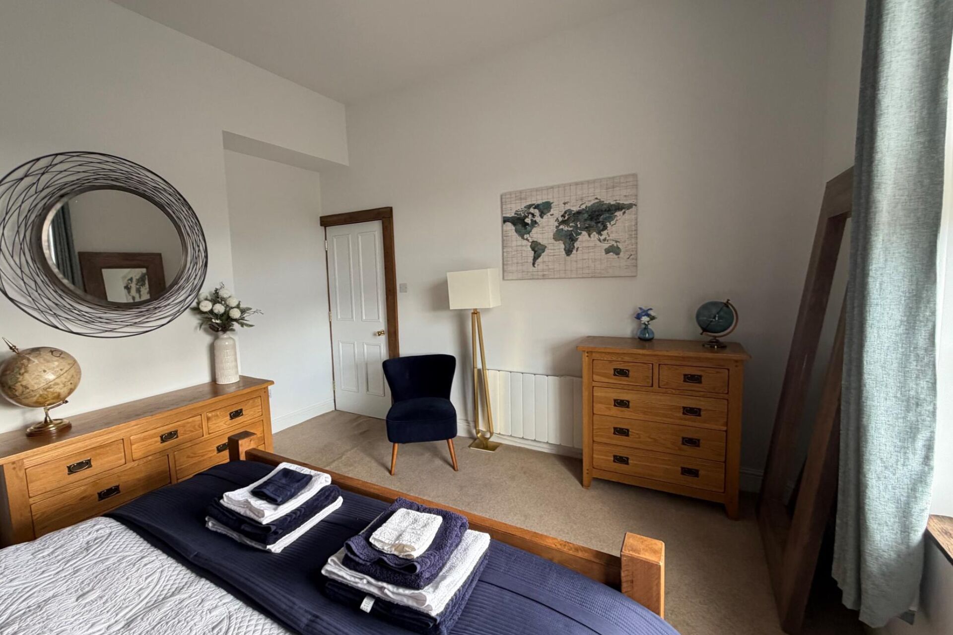 A bedroom with a bed, a dresser, a chair, a lamp, a globe, and a world map on the wall.