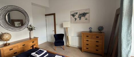 A bedroom with a bed, a dresser, a chair, a lamp, a globe, and a world map on the wall.