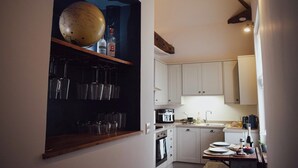 A kitchen with white cabinets, a wooden shelf with glasses, a globe, and a table with plates and a bottle.