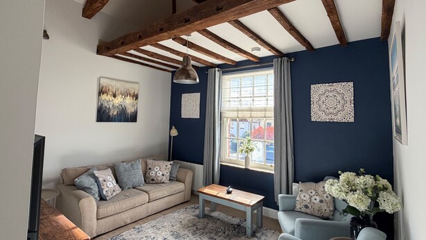 A living room with a high ceiling, wooden beams, a sofa, a coffee table, a TV, and a window with curtains.